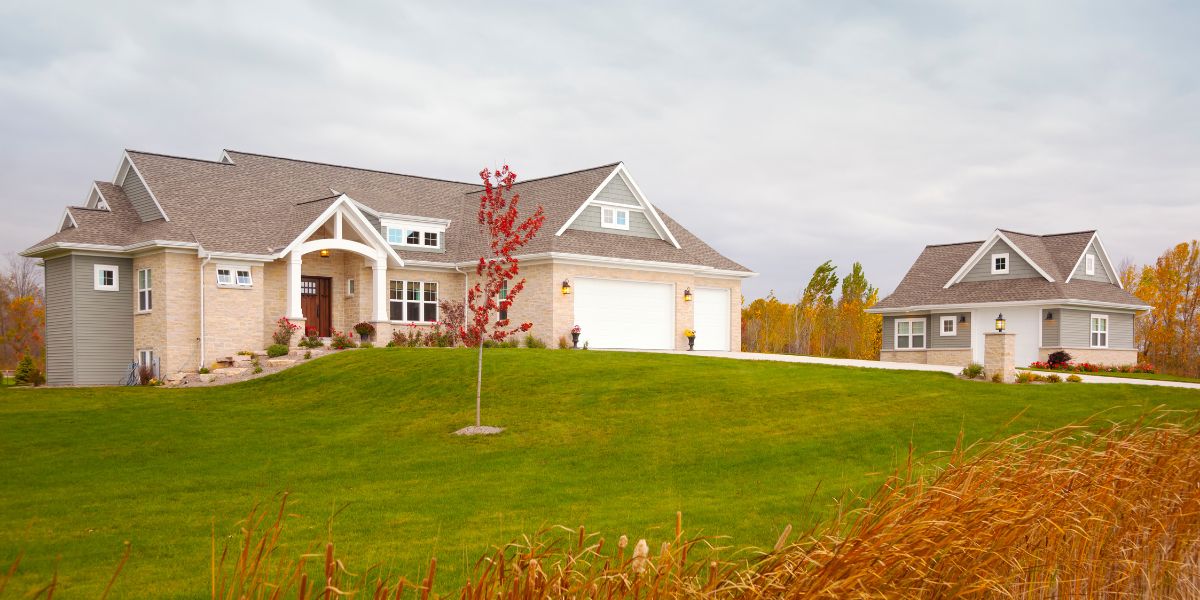 Large ranch-style house with detached garage on spacious lawn.