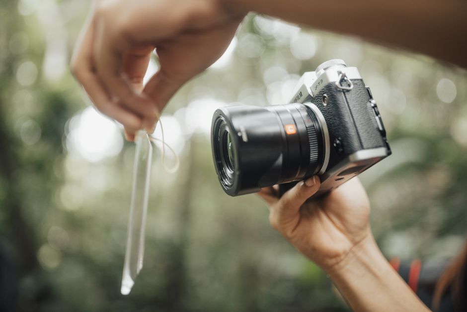 A focused, clean shot of a photographer's hands meticulously cleaning a professional camera body and lens with specialized tools, representing gear maintenance and professionalism.