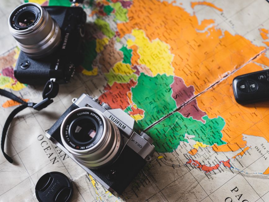 Professional photographer sits at a desk with a camera and a laptop displaying a digital map, illustrating the process of ...